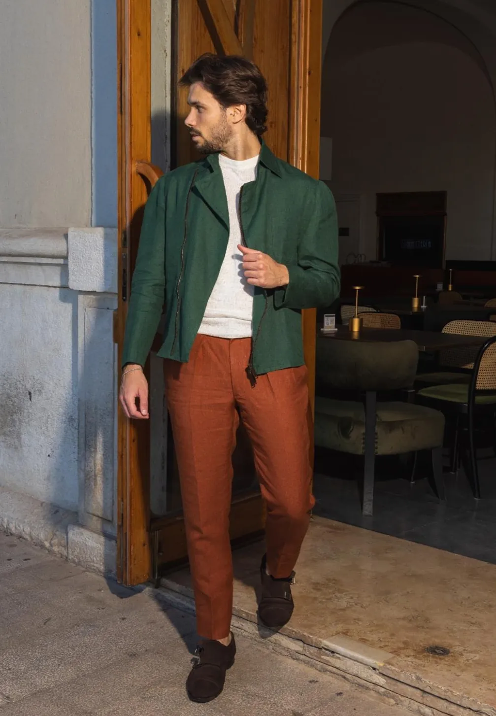 Green Vibe jacket and rust trousers in a doorway